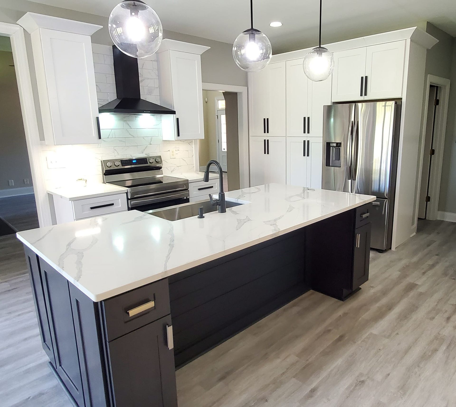 A modern kitchen featuring white cabinets, a dark gray island with white marble countertops, and stainless appliances.