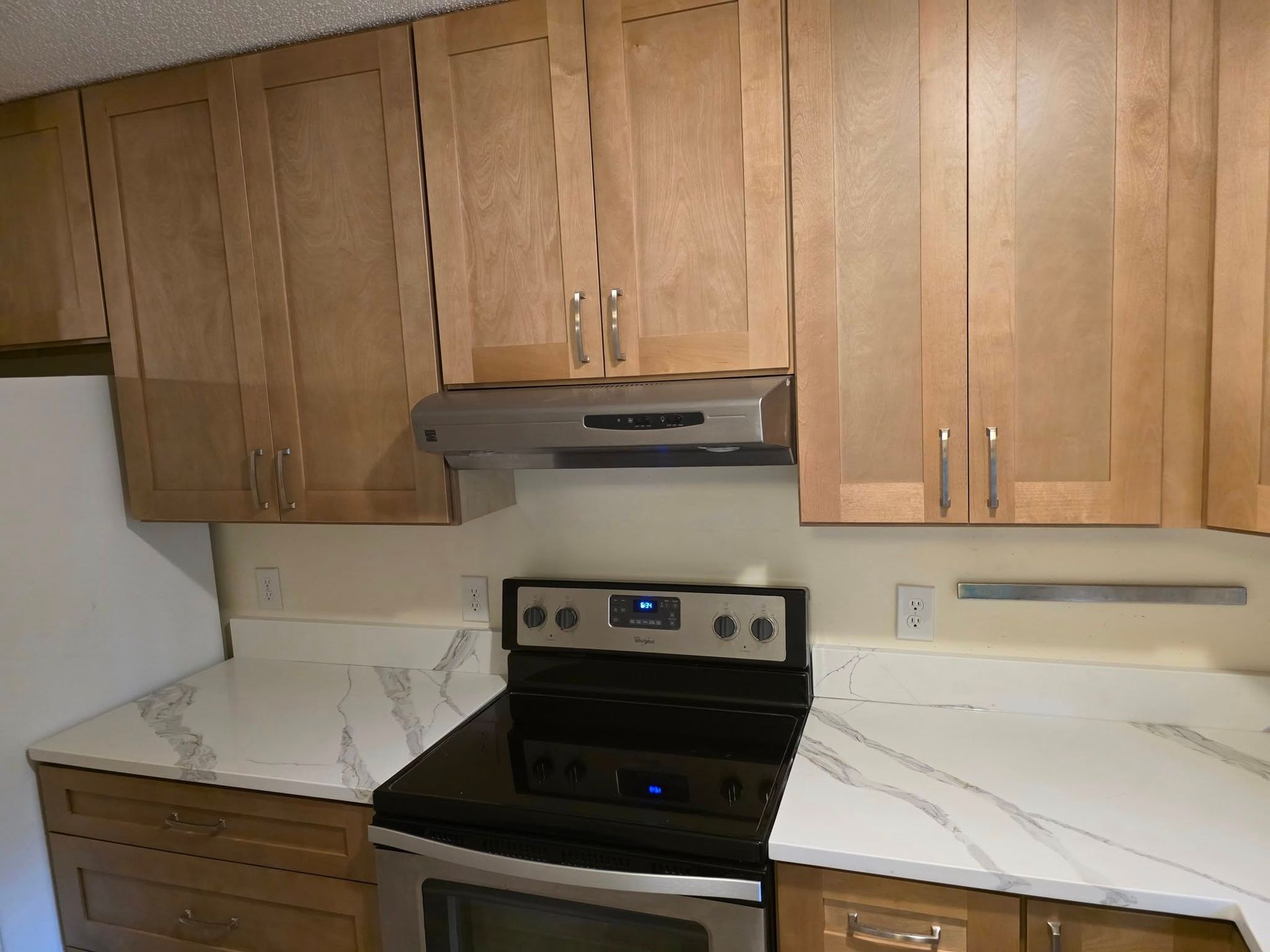 Kitchen counter with wood cabinets and a stainless steel stove, range hood, and white marble-style countertop.