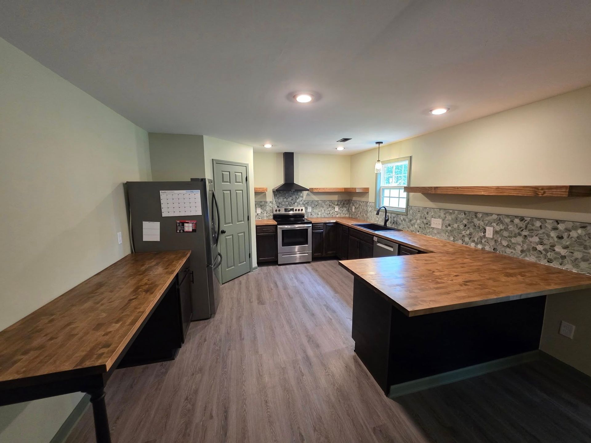 A renovated kitchen featuring dark cabinets, light wood countertops, a grey door, and a stainless steel range and fridge.