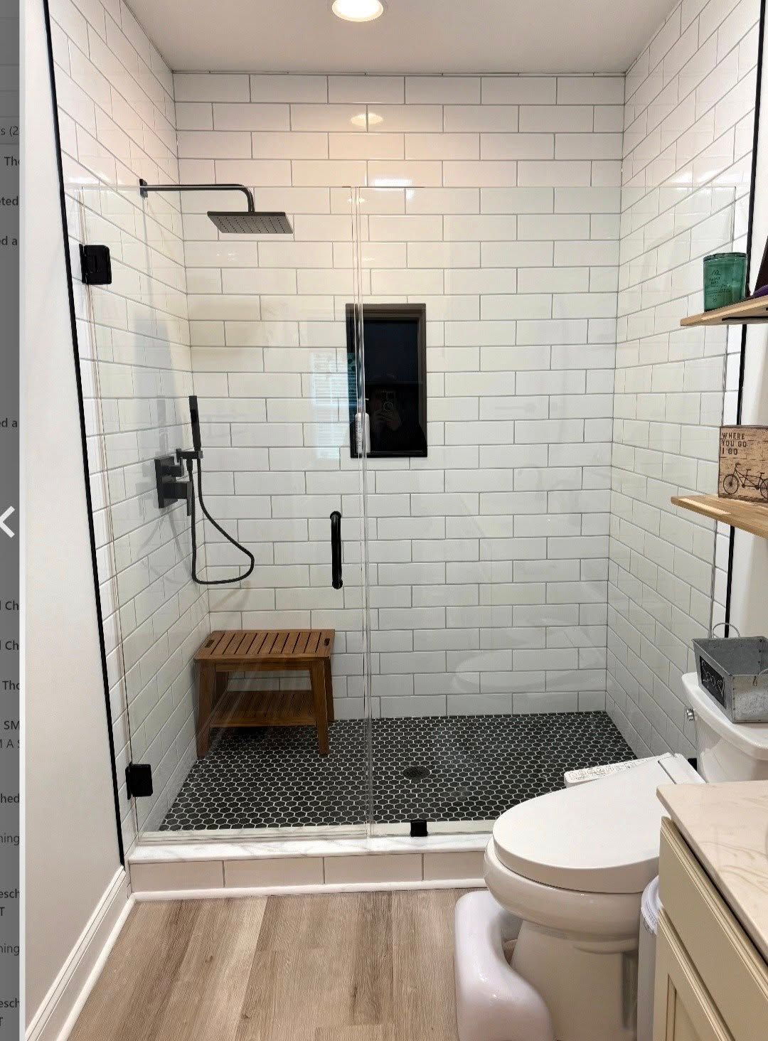A modern bathroom shower with white subway tile walls, a dark pebble floor, glass door, and a wooden bench seat.