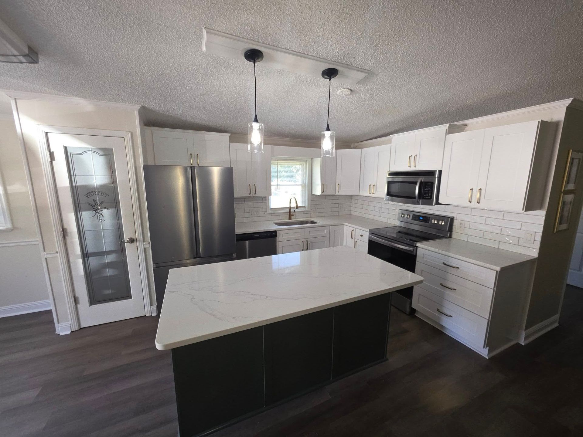 A modern kitchen featuring a dark island with a white countertop, white cabinets, stainless appliances, and wood flooring.