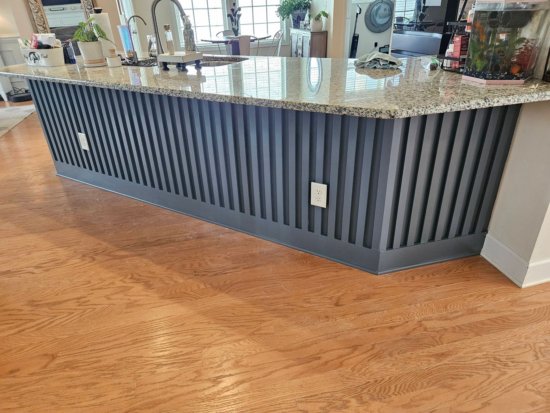 A kitchen island featuring a dark grey, vertical slat design on the front, set against light brown hardwood flooring.