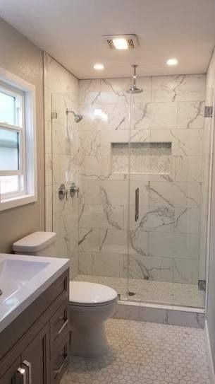 A modern bathroom featuring a white marble-tiled walk-in shower with a glass door, next to a white toilet and vanity.