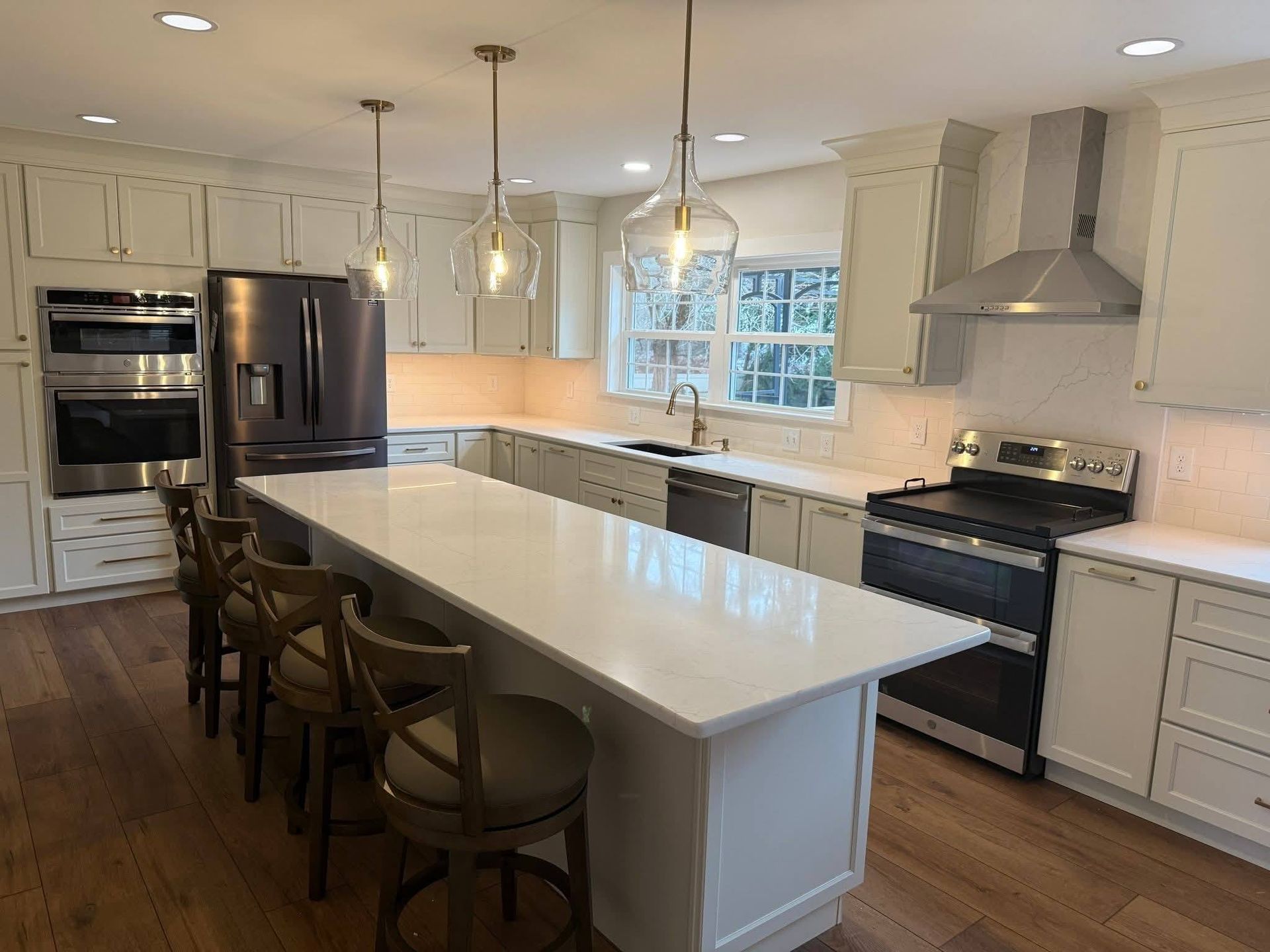 A modern kitchen featuring white cabinets, stainless steel appliances, a large central island, and three pendant lights.