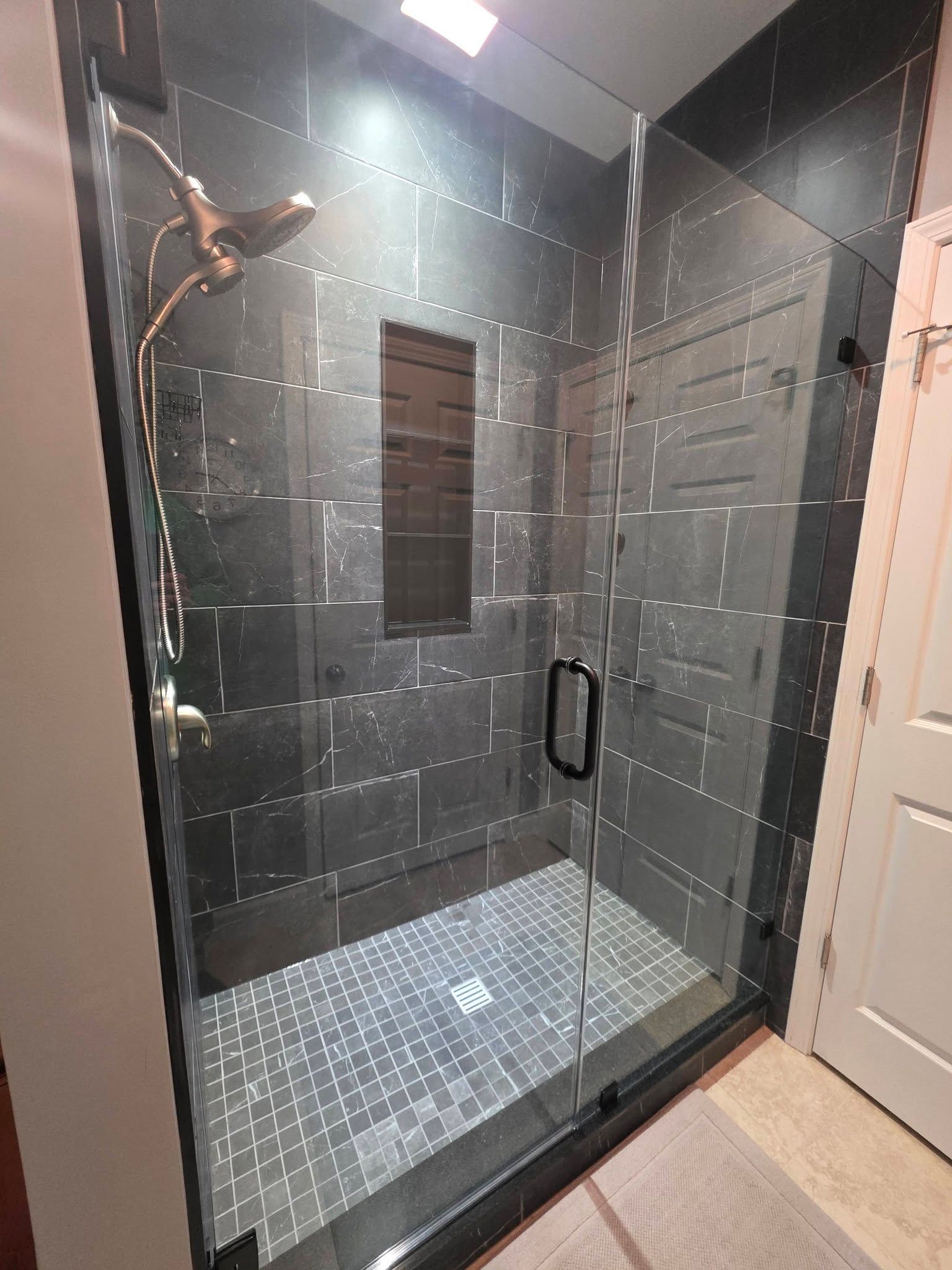 A glass-enclosed shower with dark gray tiled walls, a small recessed niche, and a metallic showerhead.