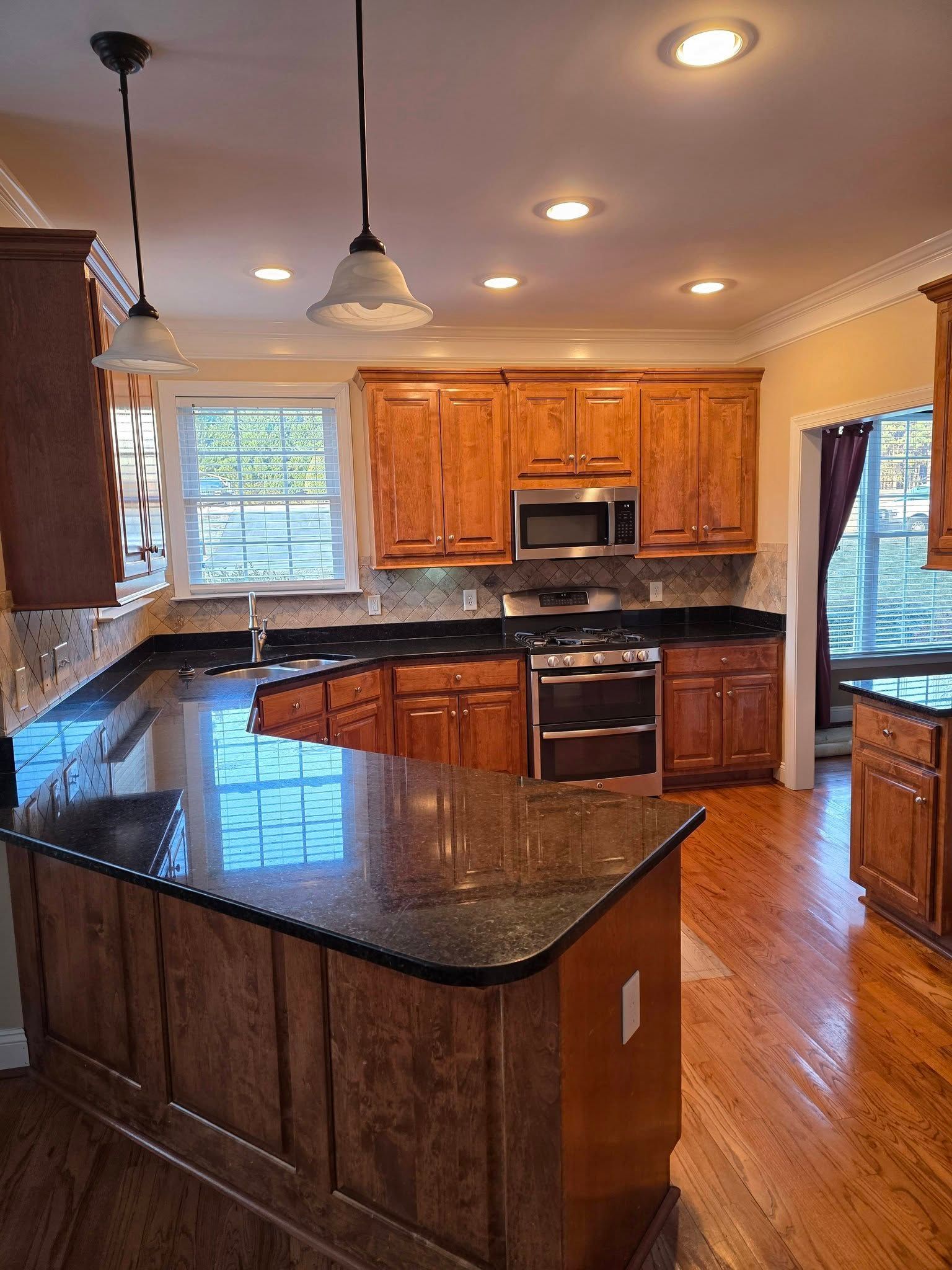A kitchen with wood cabinets, dark granite countertops, stainless steel appliances, and two pendant lights overhead.