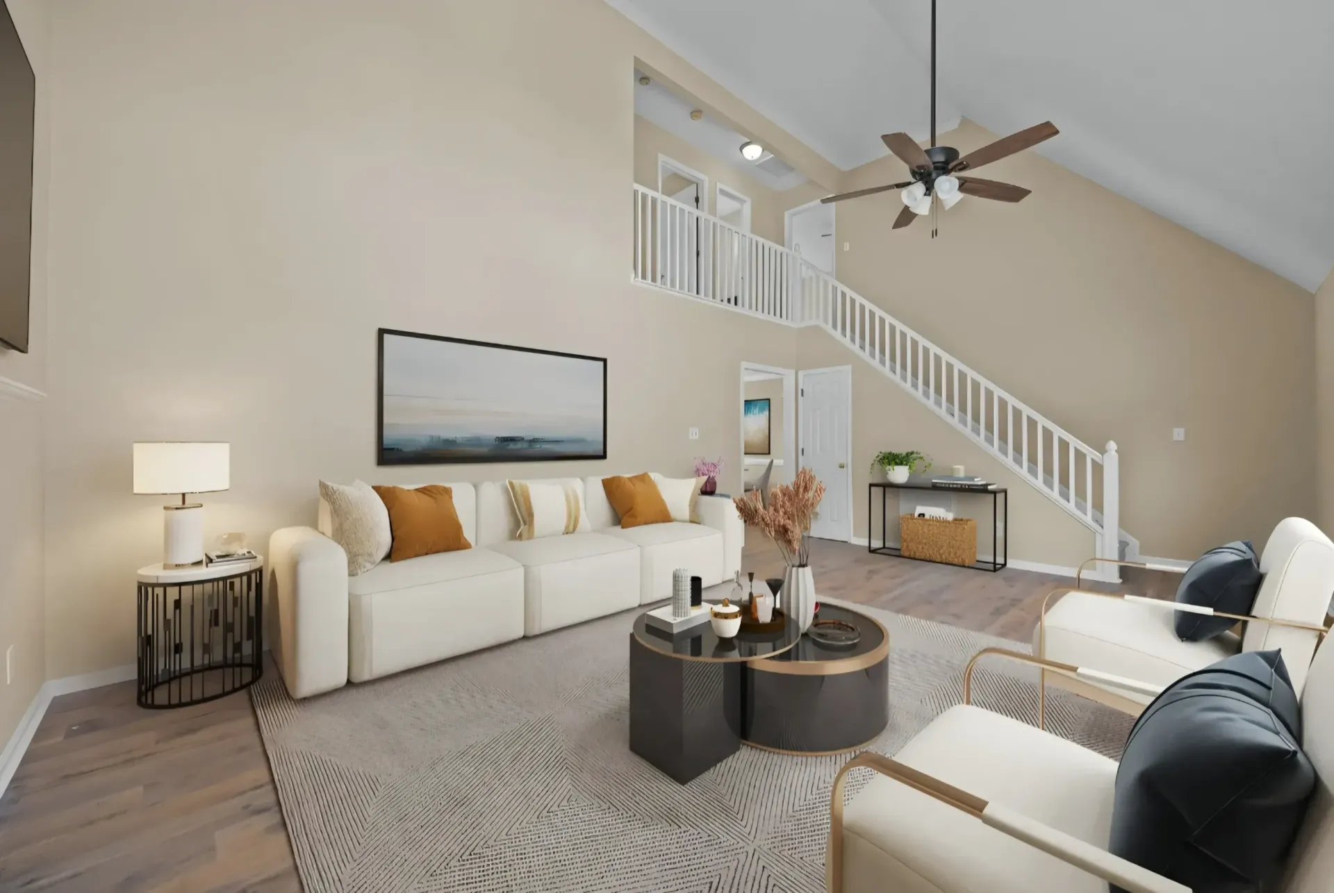 A bright living room with a white sofa, two armchairs, a patterned rug, a round coffee table, and a staircase.