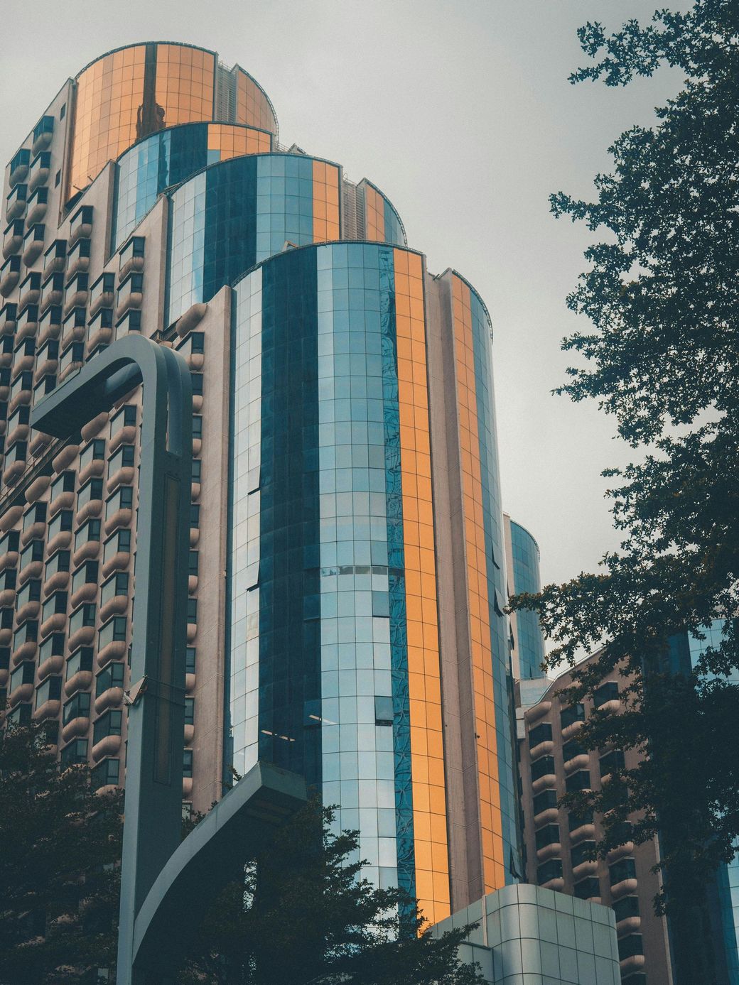 Tall skyscraper with mirrored facade, reflecting surrounding buildings and sky, with a hint of gold and blue.