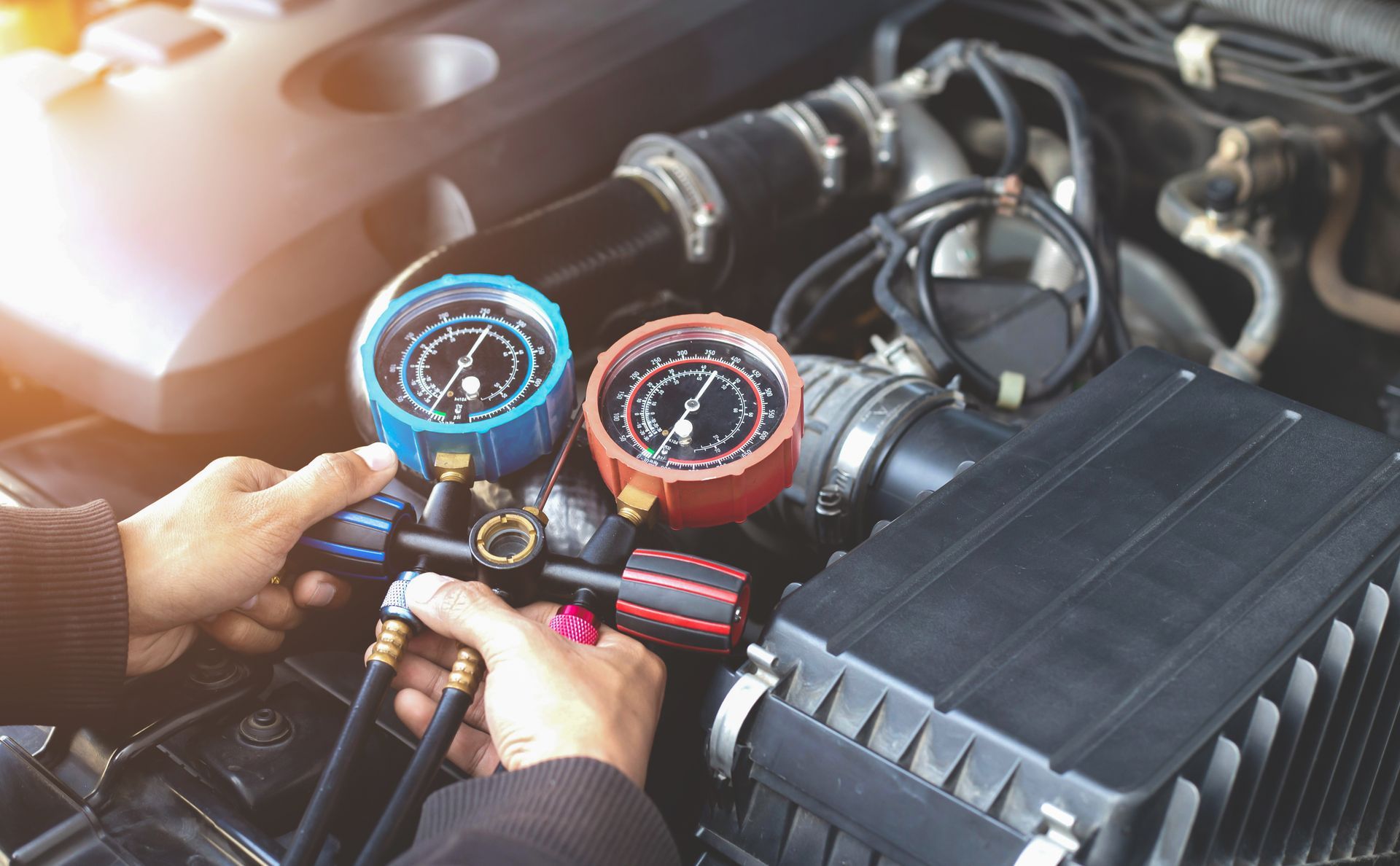 A mechanic using AC pressure gauges to service a car air conditioner. A mechanic using AC pressure gauges to service a car air conditioner.