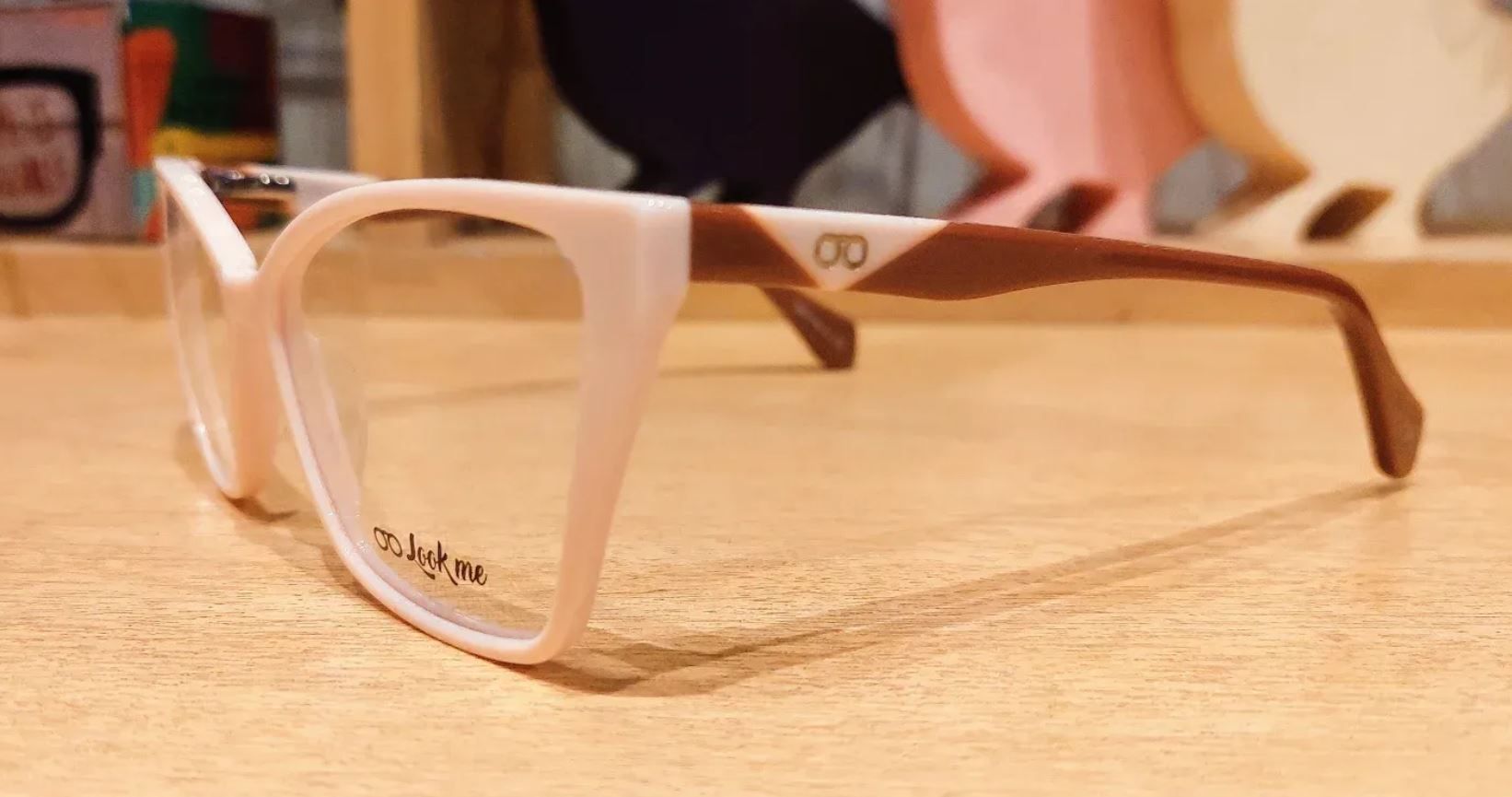 Gafas con montura blanca y patillas marrones descansando sobre una mesa de madera.