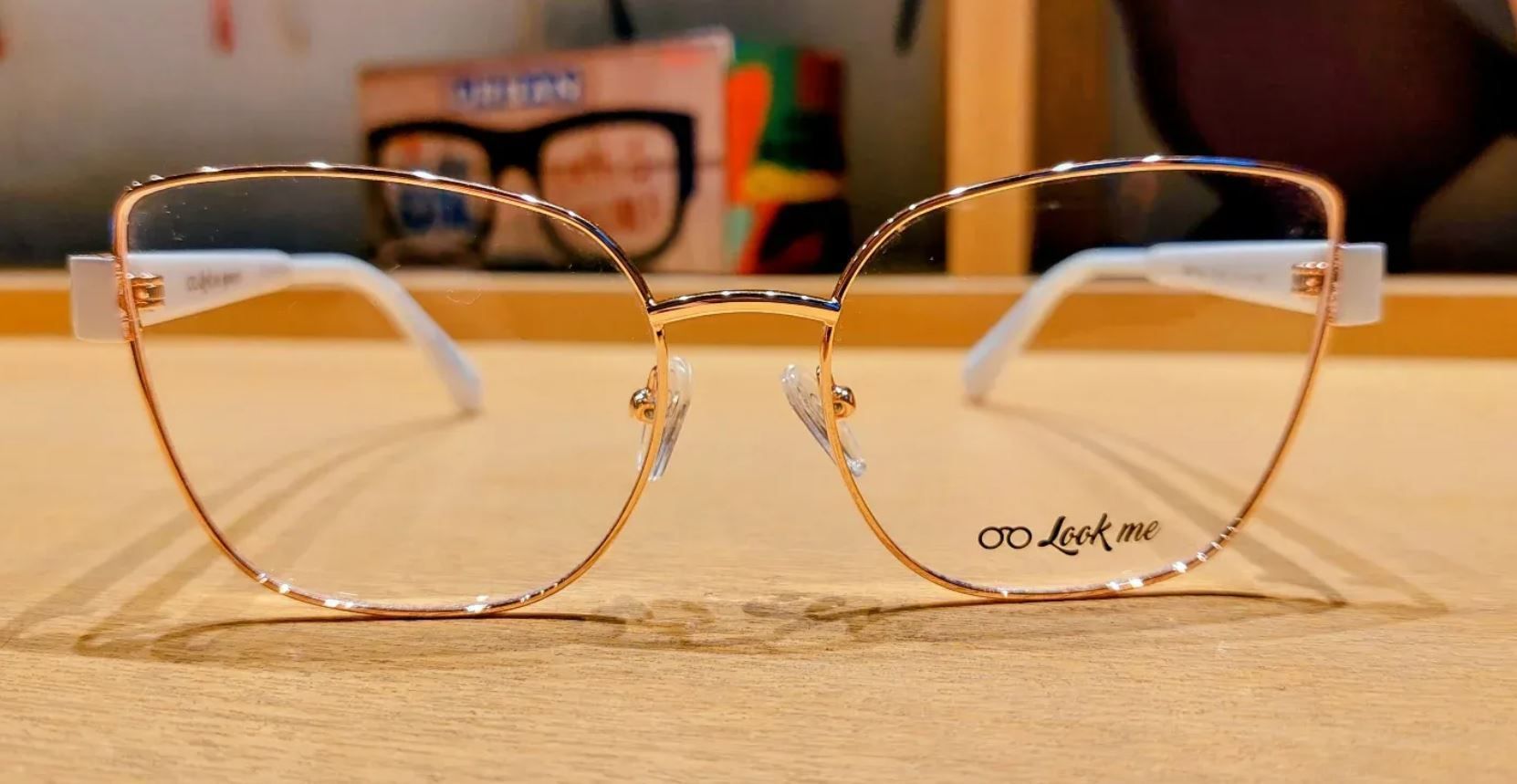 Unas gafas con montura de alambre dorado descansan sobre una mesa de madera con un fondo difuminado de tonos cálidos.