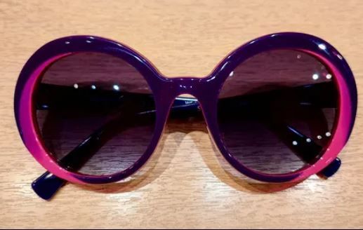 Gafas de sol redondas moradas sobre una superficie de madera.