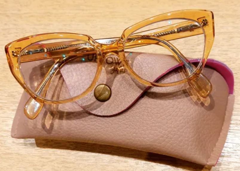 Gafas de sol ámbar estilo ojo de gato sobre un estuche rosa con un paño redondo para lentes.