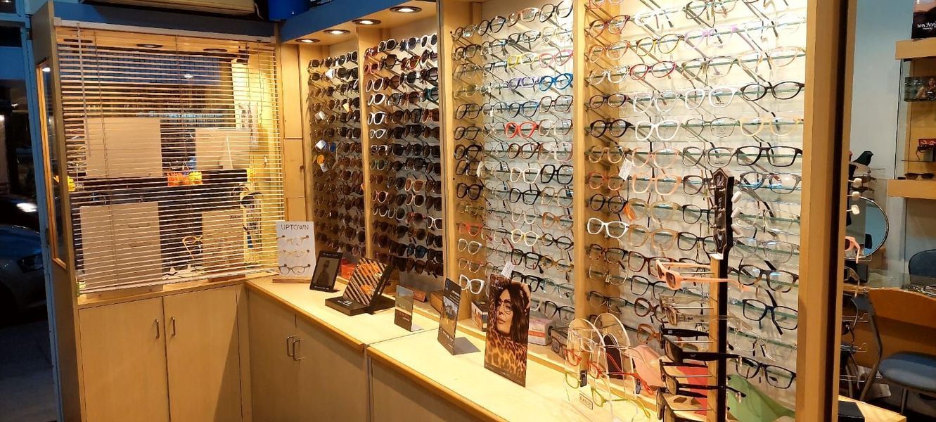 Exhibición de una óptica con filas de gafas en estantes de pared y mostradores bajo iluminación cálida.