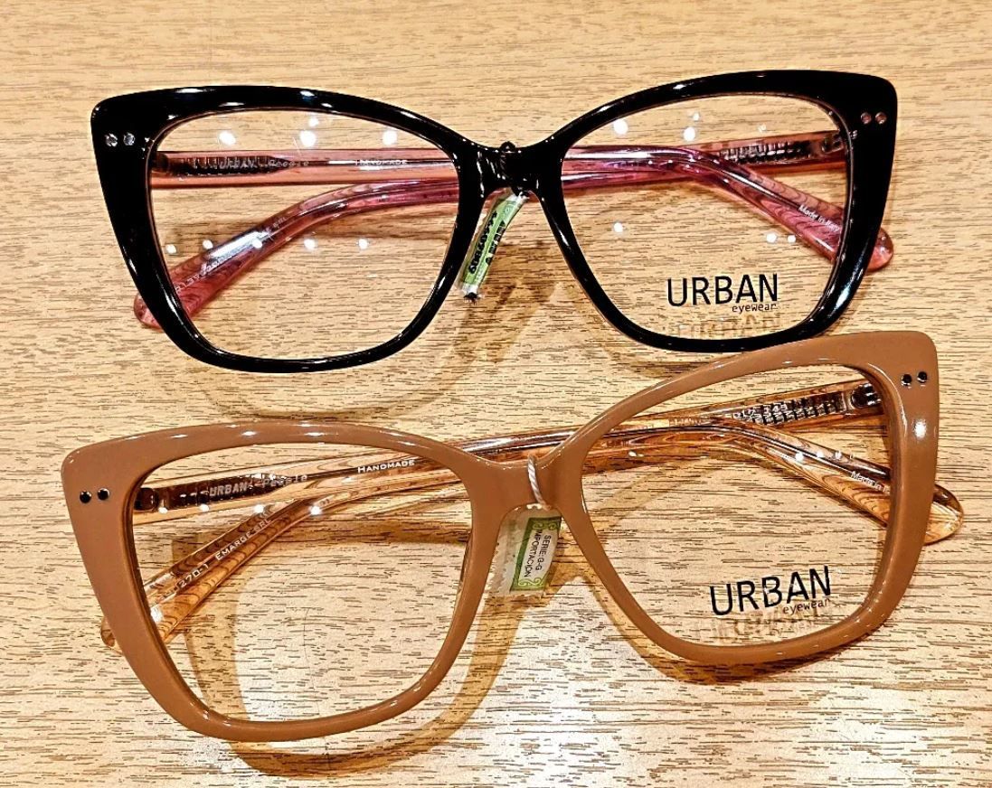 Dos monturas de gafas URBAN, negras y color canela, expuestas sobre una superficie de madera texturizada.