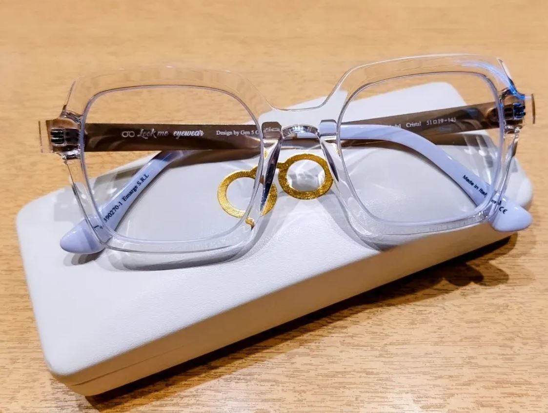 Gafas transparentes con detalles dorados sobre un estuche blanco en una mesa de madera.