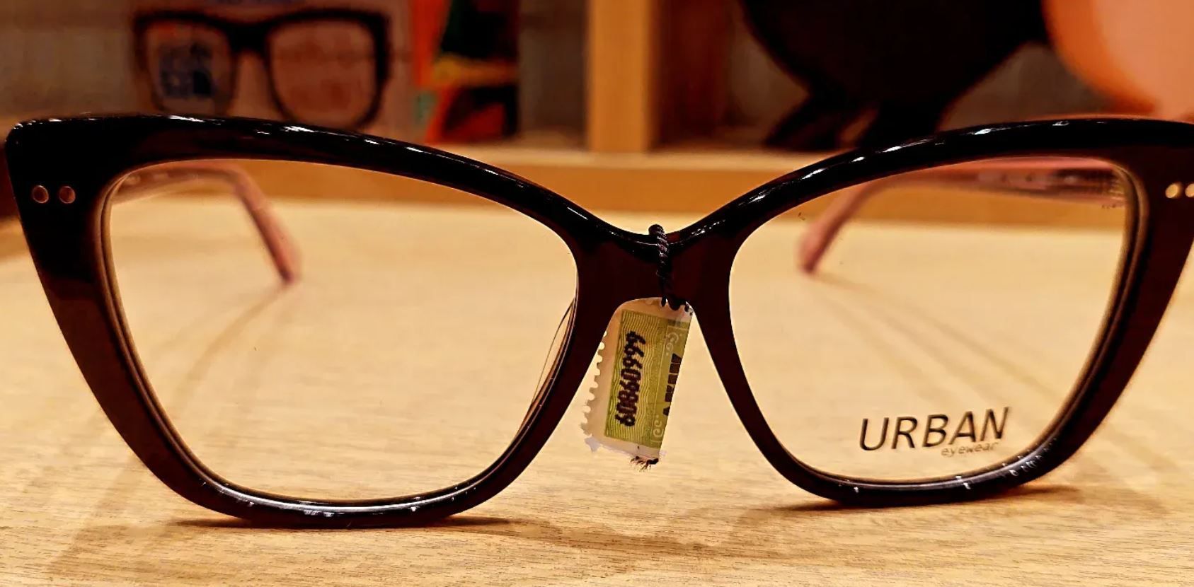 Gafas negras con lentes transparentes y una etiqueta de precio dorada sobre una superficie de madera.