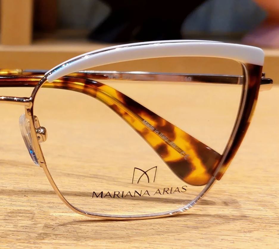 Gafas de carey y oro sobre una superficie de madera, con el logotipo de MARIA N ARIAS en la lente.