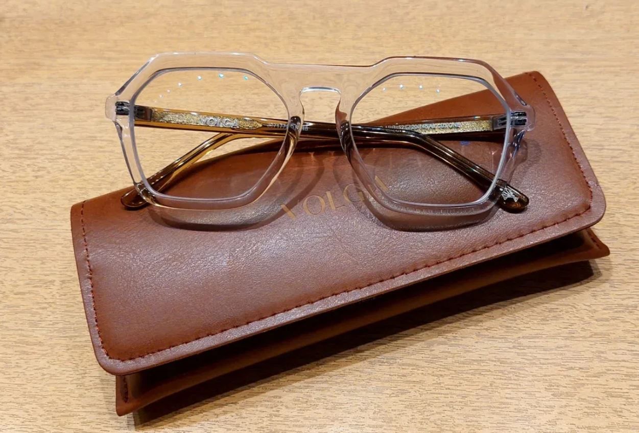 Gafas transparentes descansando sobre un estuche de cuero marrón sobre una superficie de madera.