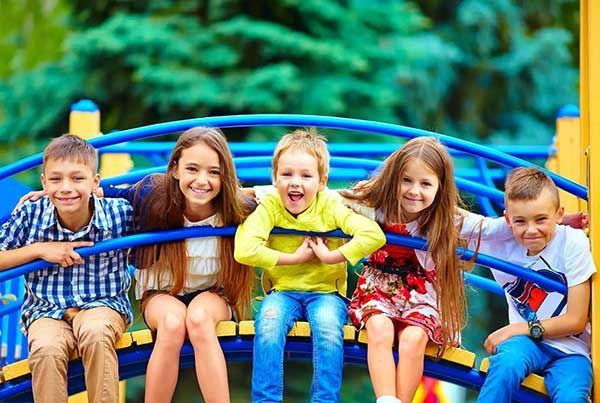 A group of children sitting on a playground toy. They are smiling.
