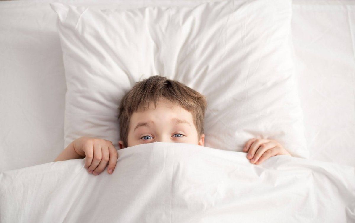 Boy in bed with cover over part of his face.