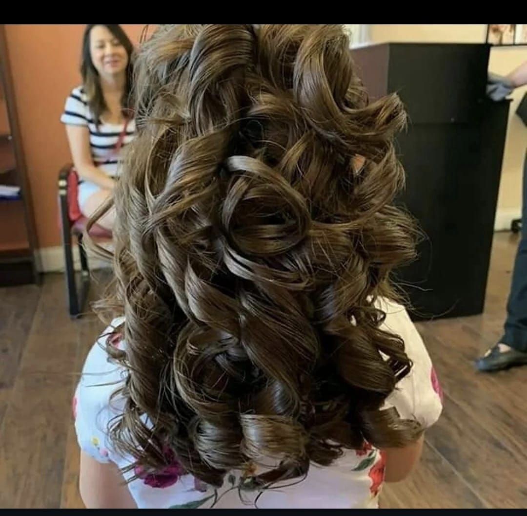 Back view of a person with long, curled brown hair in a salon chair
