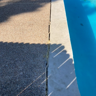 Poolside concrete deck beside blue water, with a shadow across the edge.