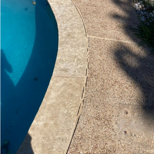Blue swimming pool beside a curved tan stone deck with dappled shadows