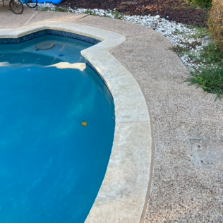 Curved backyard pool edge with blue water and a beige textured patio