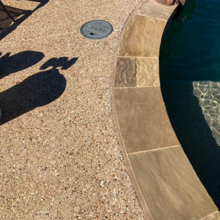 Poolside stone deck with a curved edge beside dark blue water and a round drain cover.