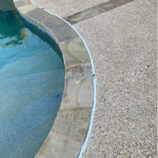 Curved pool edge with clear blue water beside a tan gravel deck