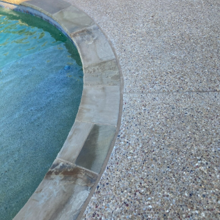 Curved stone pool edge beside blue water and speckled deck surface