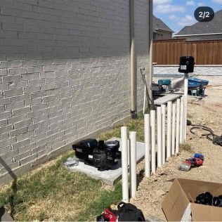 Partially installed white PVC fence posts beside a gray house wall on a construction site