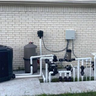 Outdoor pool equipment with white PVC pipes, pumps, and tanks against a brick wall