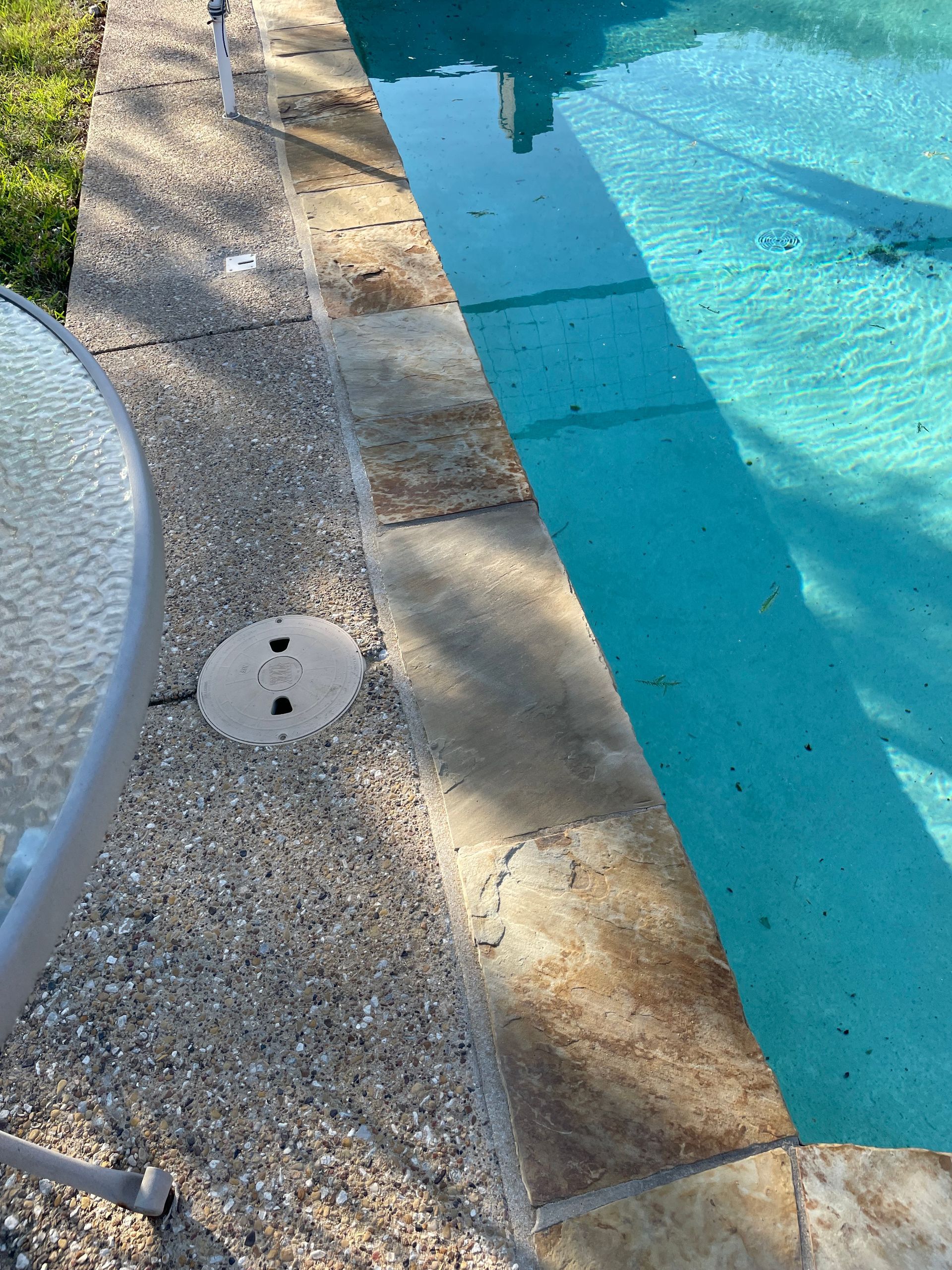 Poolside gravel walkway beside turquoise swimming pool with concrete edge and drain cover