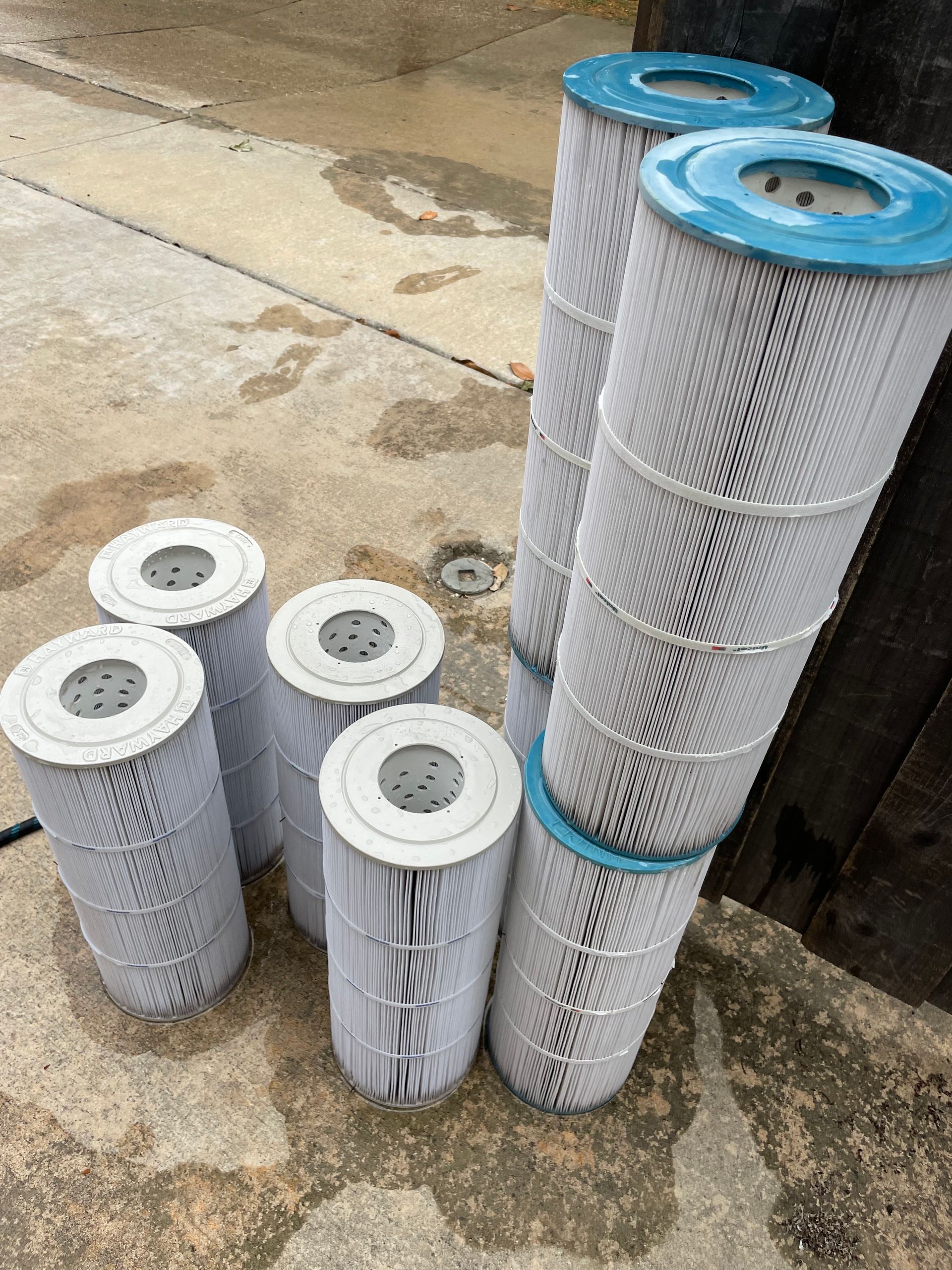Rolls of white cylindrical filter mesh stacked on a wet concrete floor, with blue-capped tops.