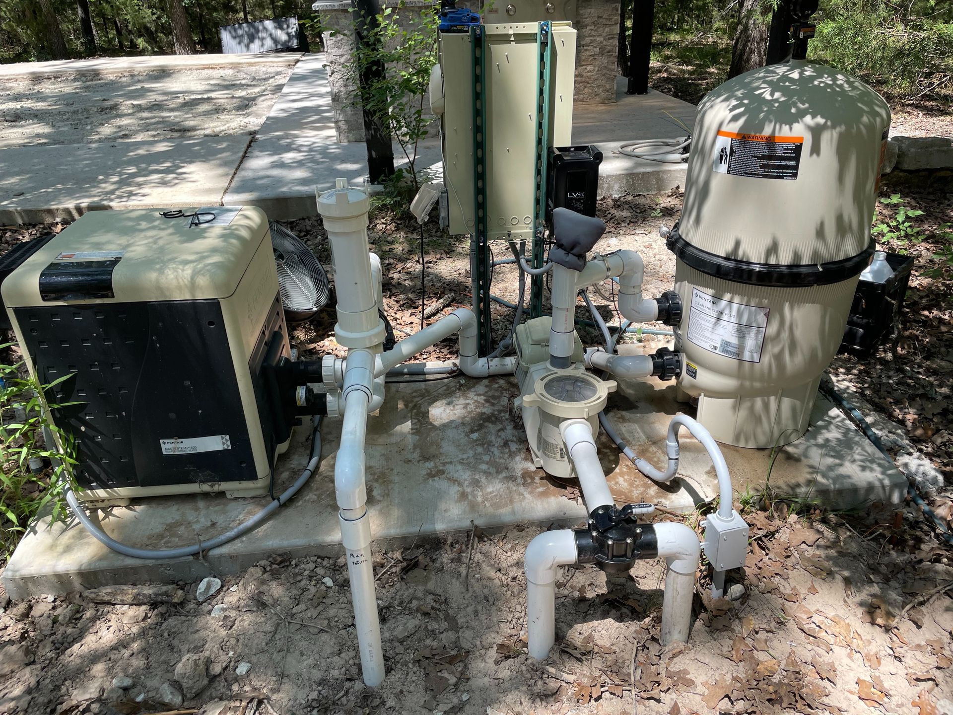 Outdoor pool equipment: pumps, filters, and white PVC piping on a concrete pad.