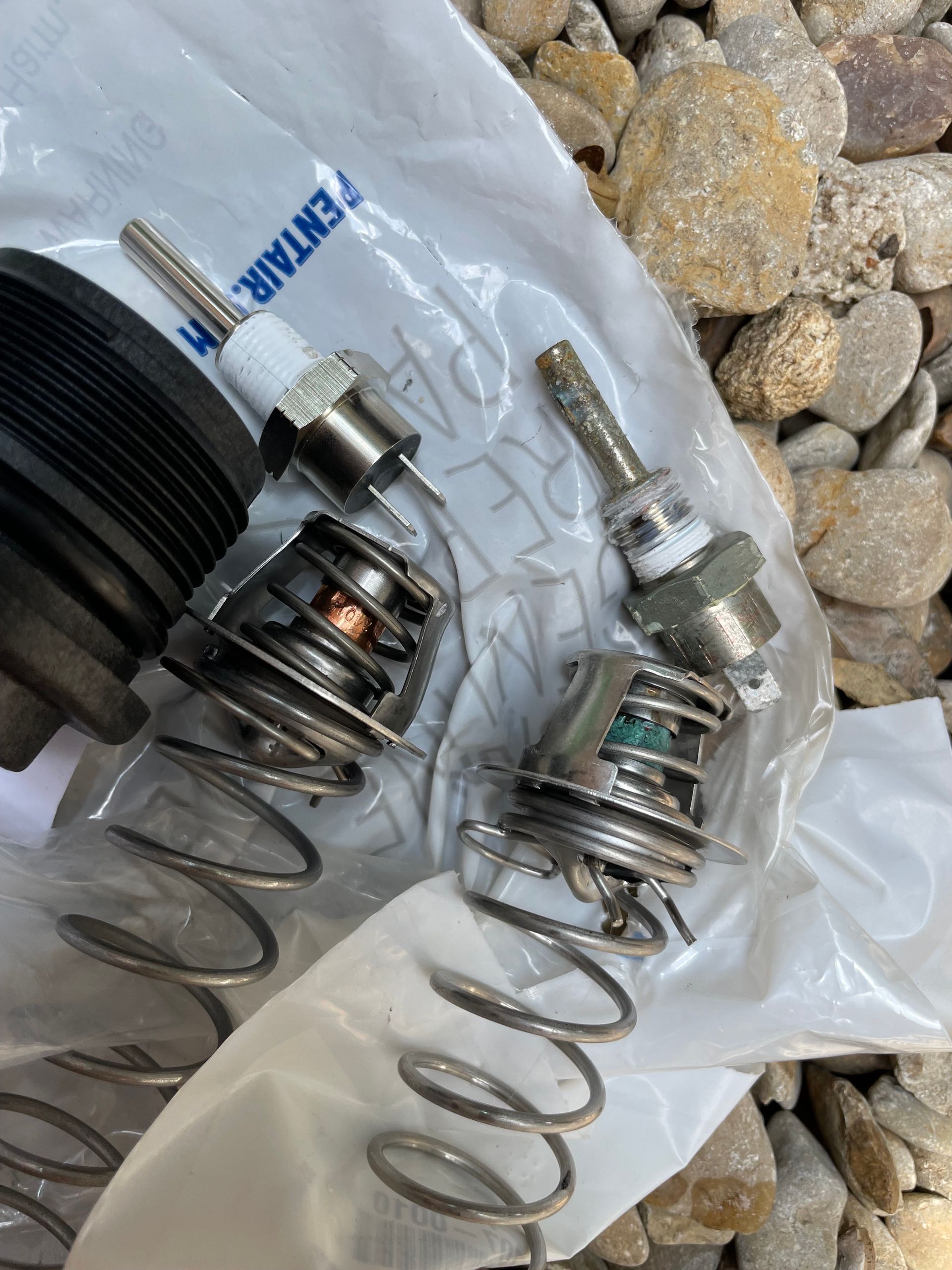 Two metal spring-loaded mechanical parts on a plastic bag over pebbles