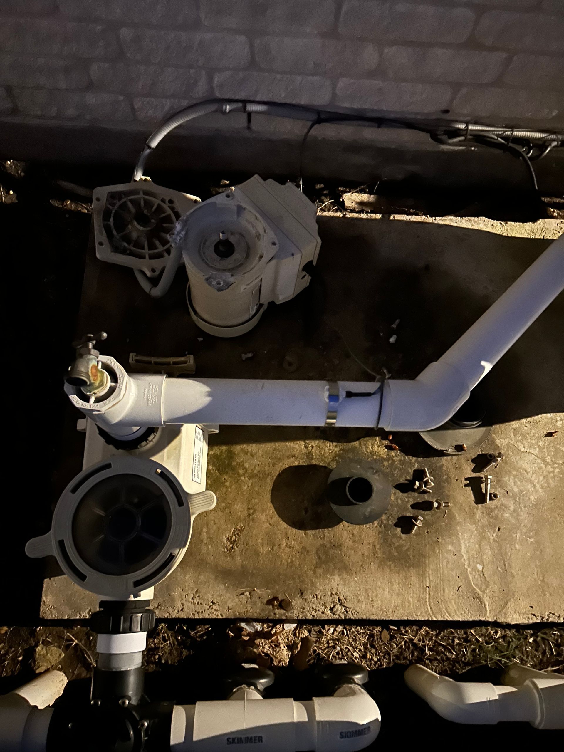 Outdoor utility pipes and valves on concrete, with a large white PVC pipe and circular fittings.