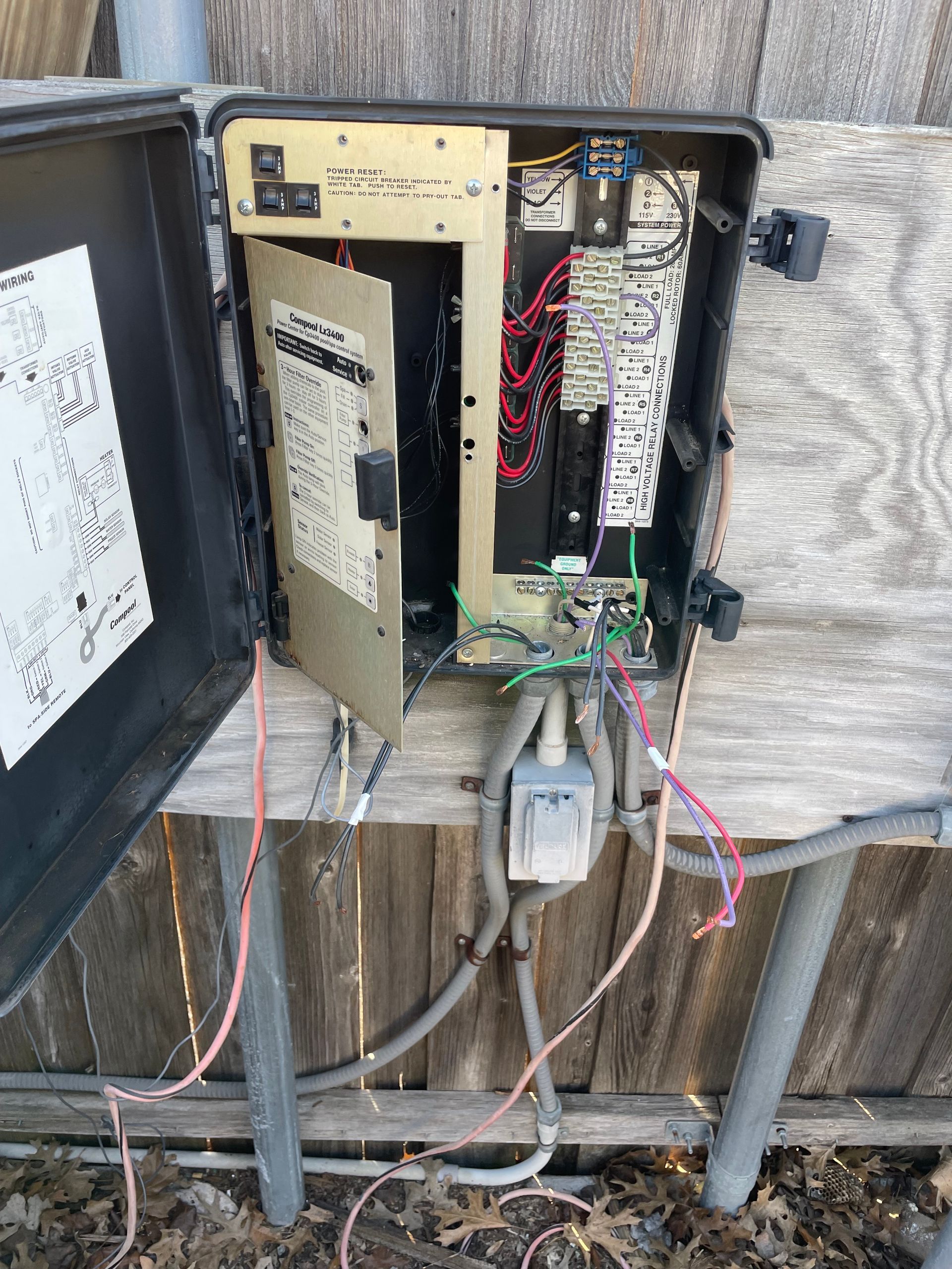 Open electrical control box with exposed wiring mounted outdoors on wooden posts.