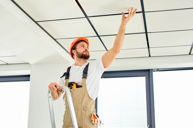 a man is standing on a ladder looking up at the ceiling