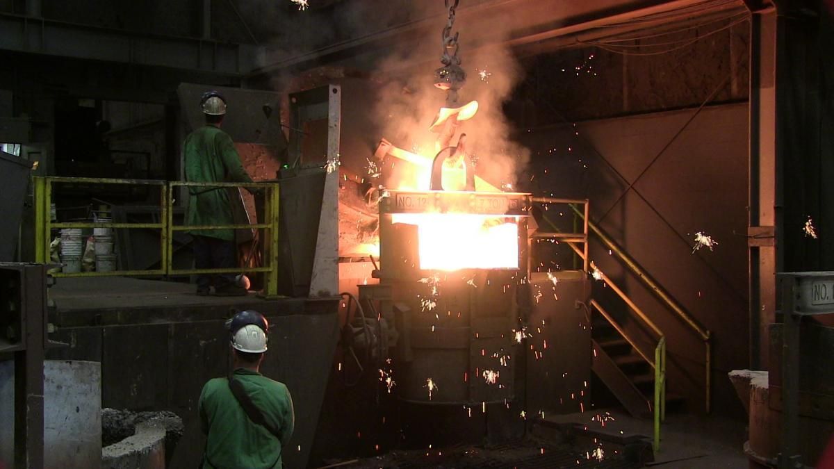 Industrial furnace with bright flames and sparks, workers nearby in a dim factory setting