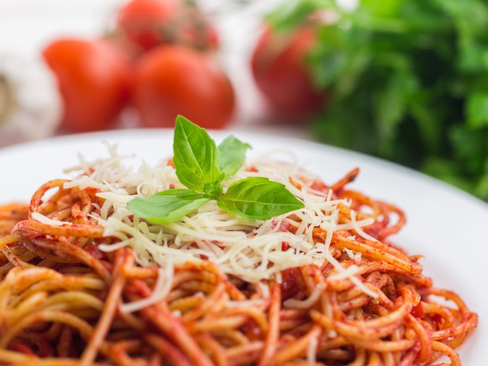 Spaghetti mit Tomatensoße, geriebenem Käse und Basilikumgarnitur auf einem weißen Teller