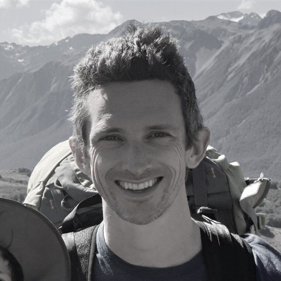 A man with a backpack is smiling in front of a mountain