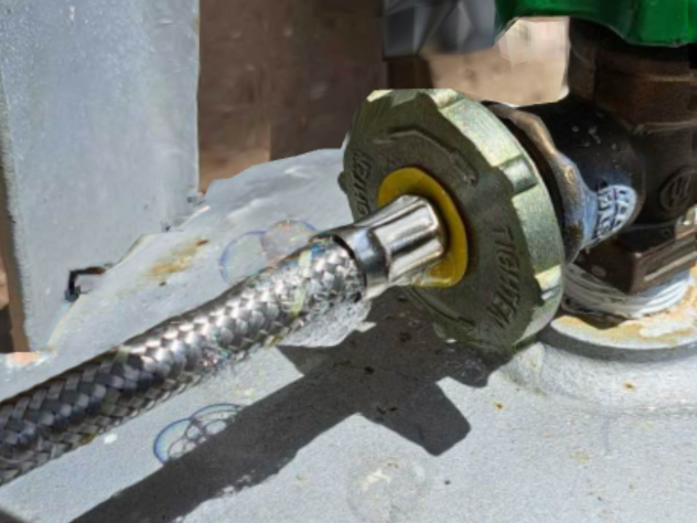 Close-up of a flexible metal gas line connected to a propane tank valve, showing yellow seal.