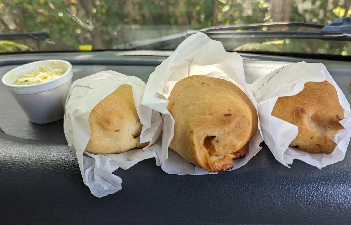 Three wrapped pastries and a cup of sauce on a car dashboard.
