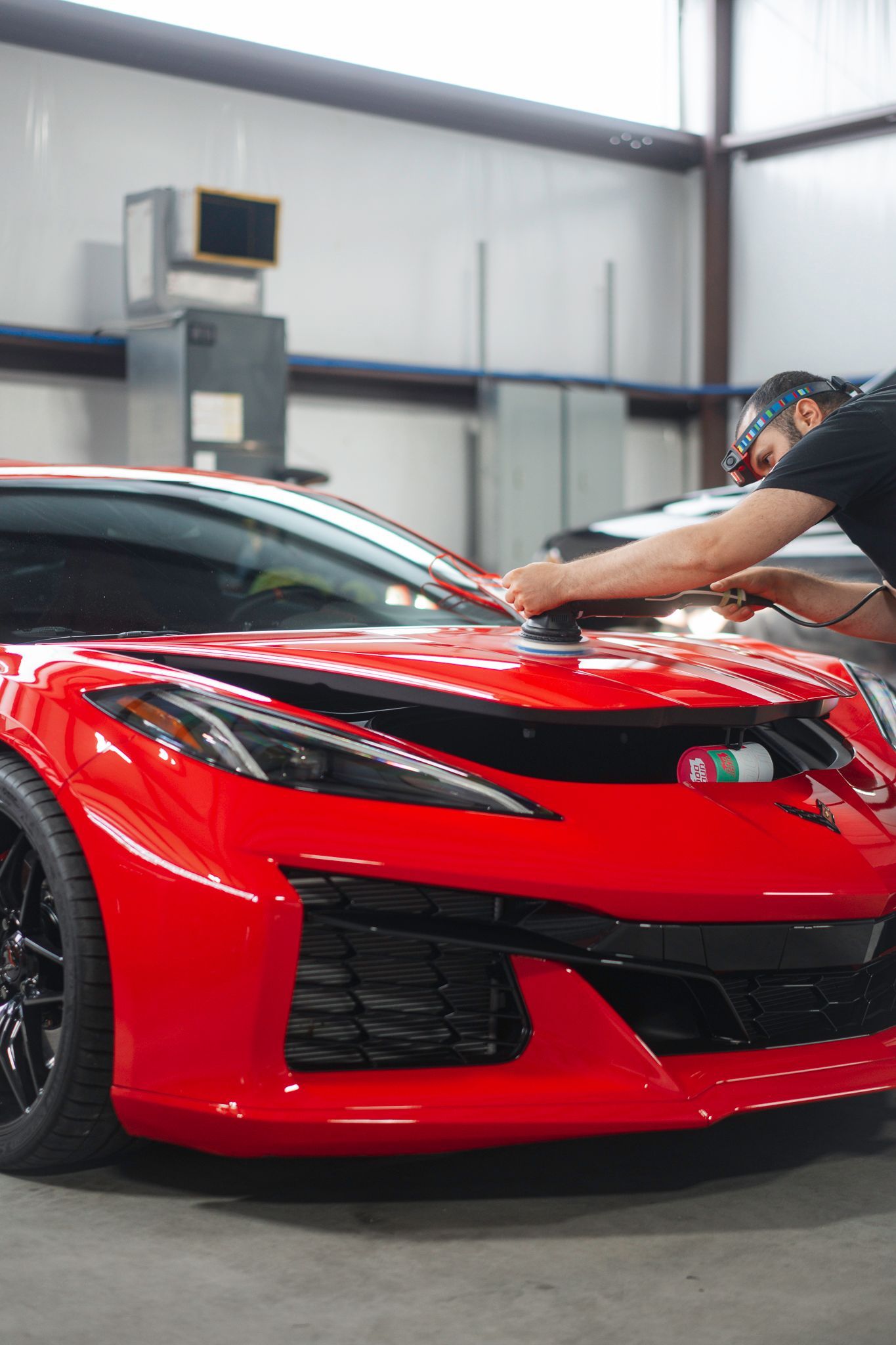 Person polishing the hood of a red sports car in a garage