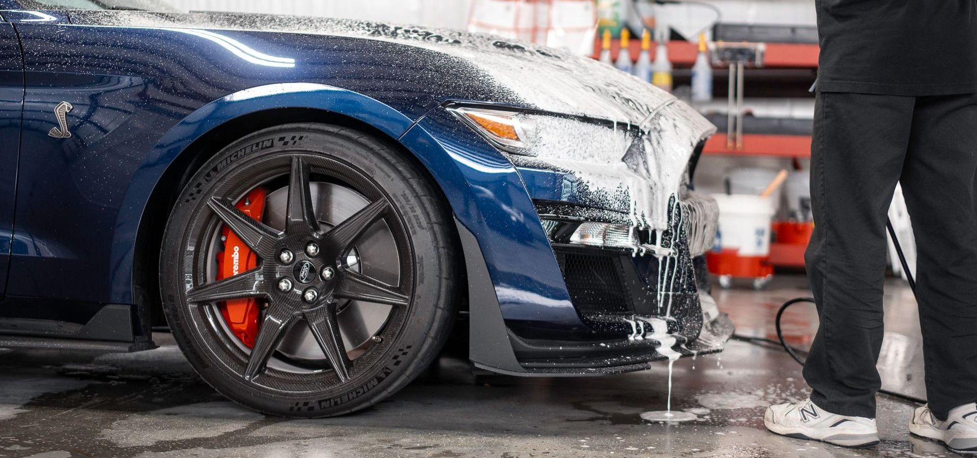 Blue sports car being washed in a garage, with a person standing beside it