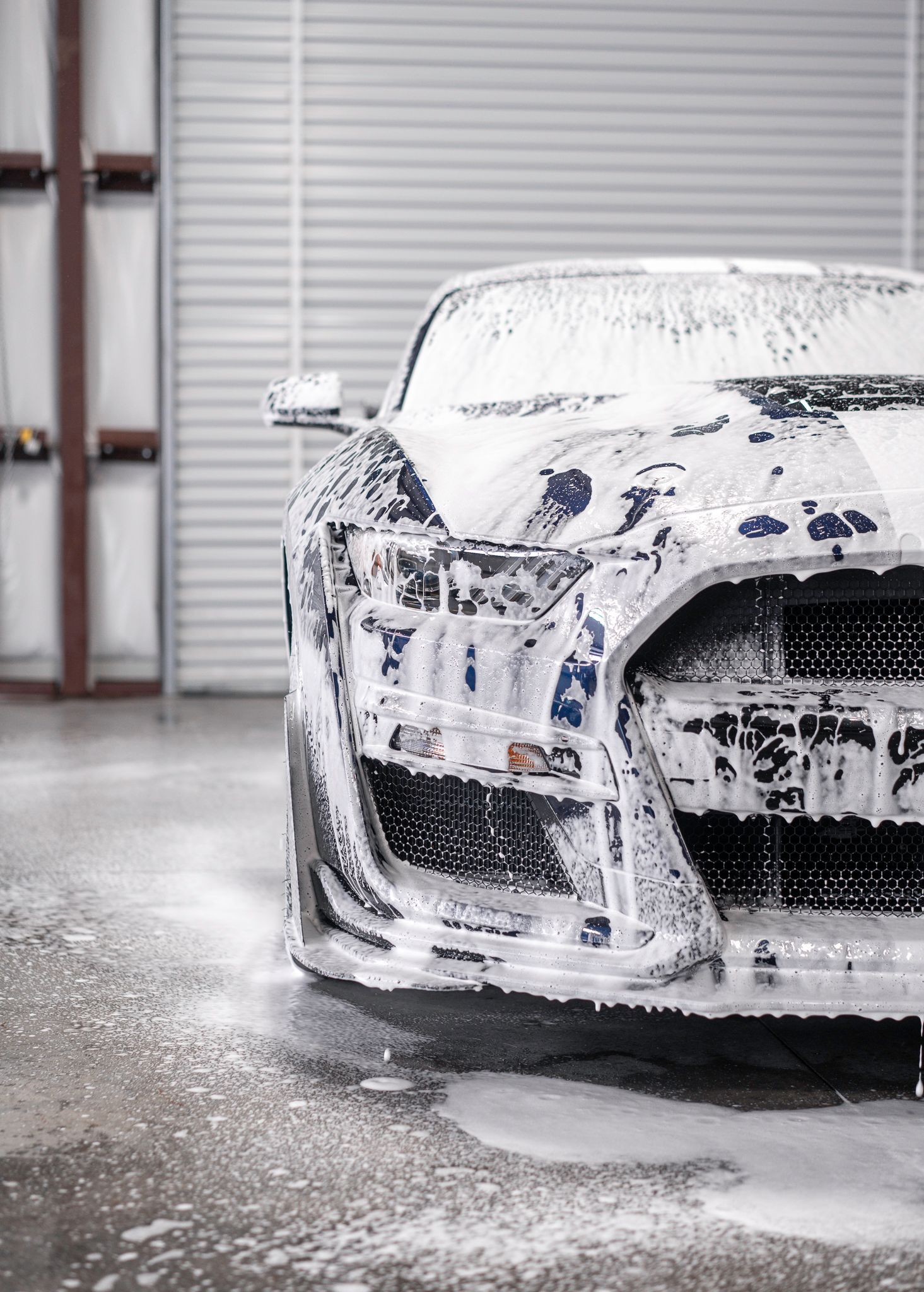 A blue sports car is covered in foam while being washed.