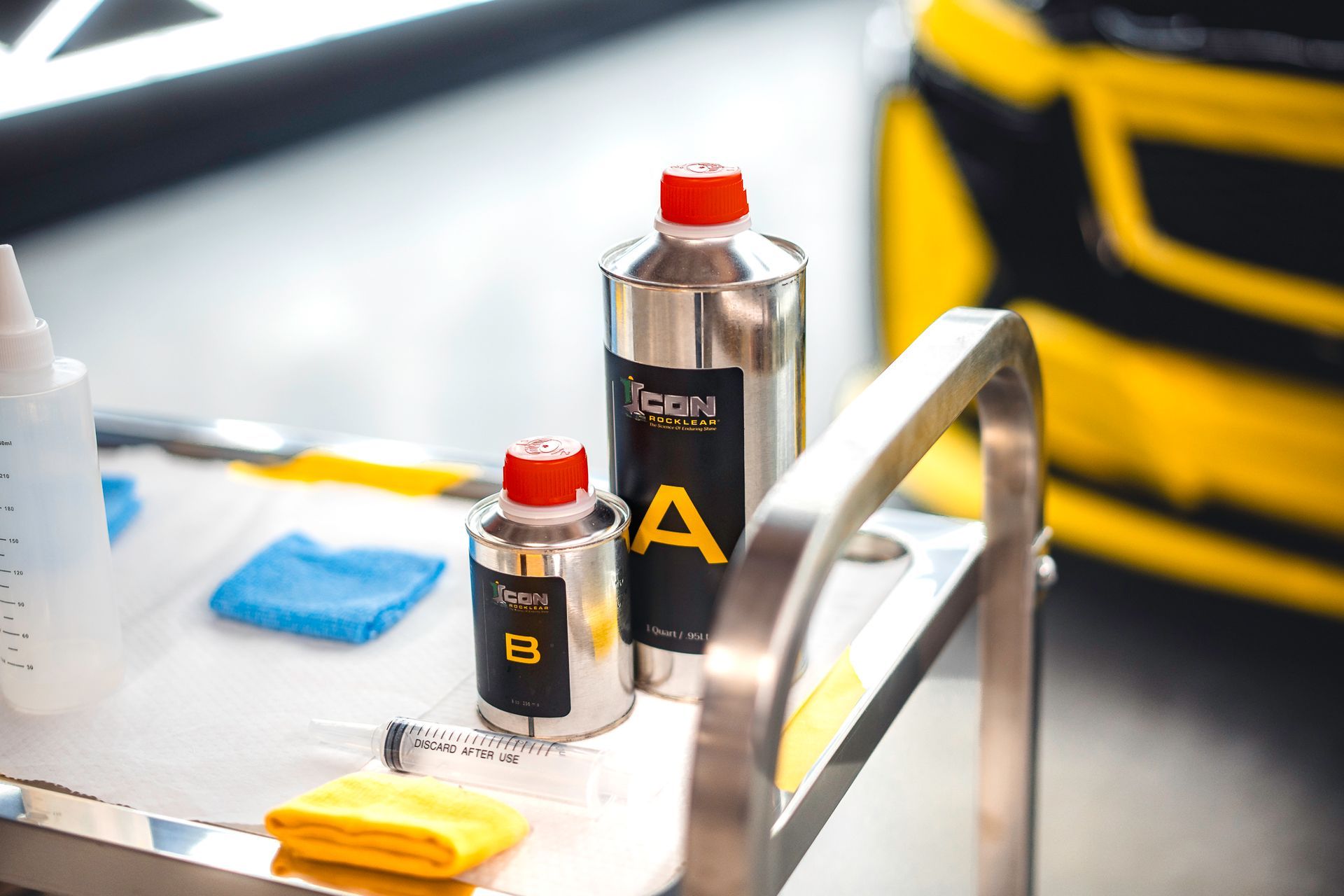 Detailing supplies on a table with bottles, towels, and a yellow car in the background